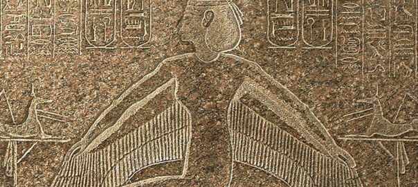 Ancient Egyptian relief of a winged humanoid figure with outstretched feathered wings, surrounded by hieroglyphs carved in stone.