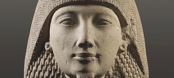 Bust of an ancient Egyptian pharaoh wearing a striped nemes headdress, in a stone statue.