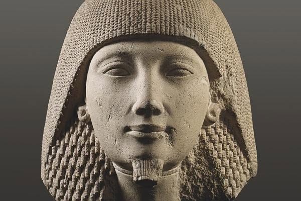 Bust of an ancient Egyptian pharaoh wearing a striped nemes headdress, in a stone statue.