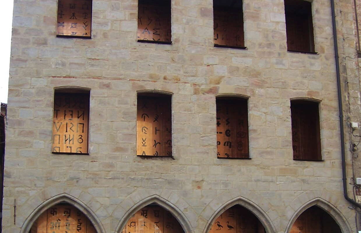 Stone building with boarded-up windows displaying dark symbols; arched ground-floor storefronts.**