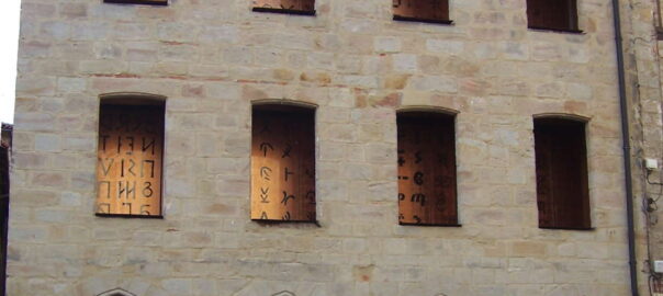 Stone building with boarded-up windows displaying dark symbols; arched ground-floor storefronts.**