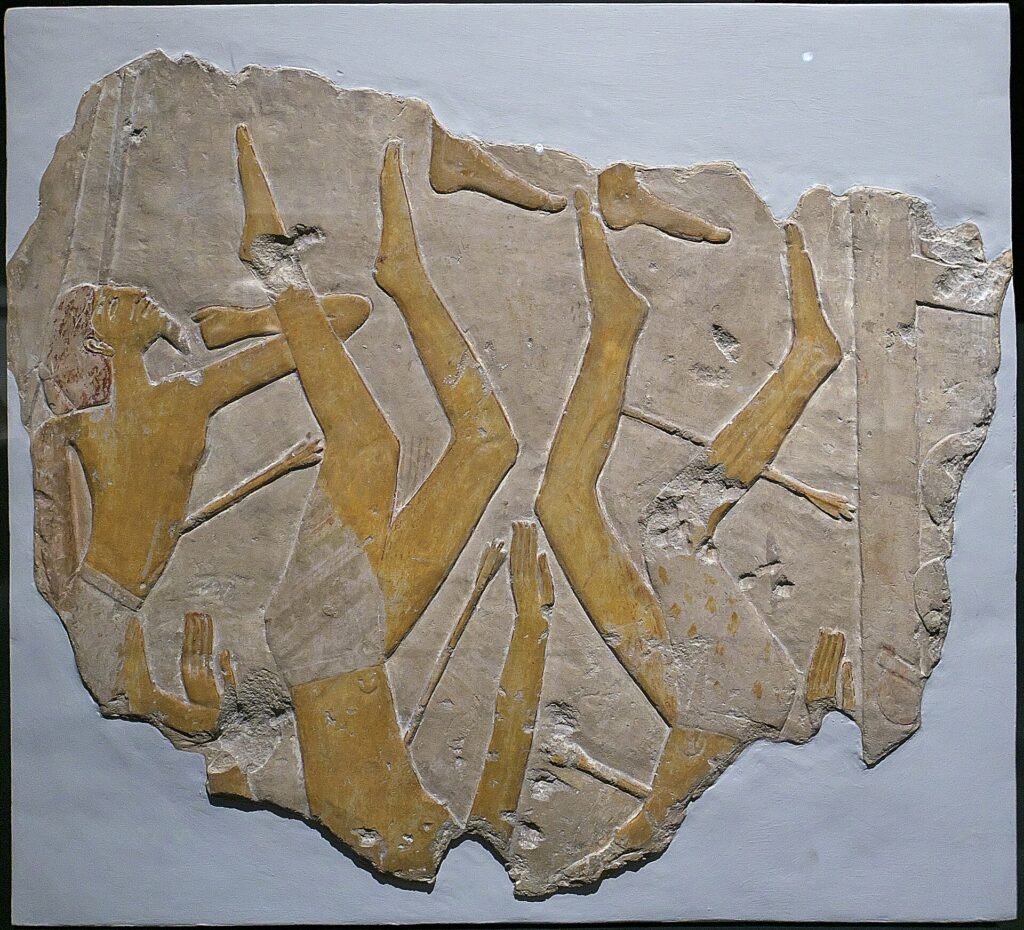 Stone relief sculpture with many elongated arms and legs extending upward from a rough rock surface.